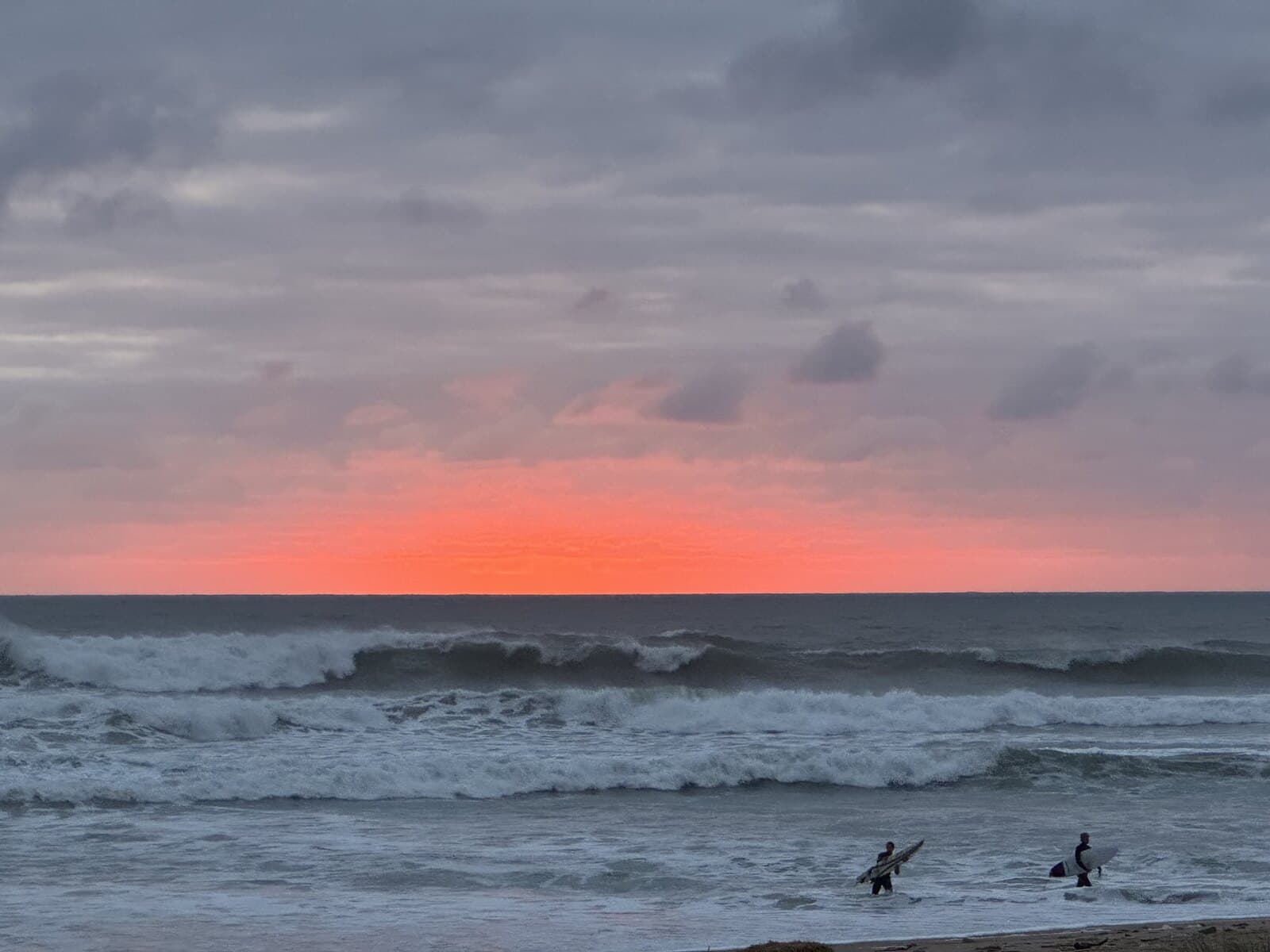Two surfers walking into the sea at sunset, Ericeira